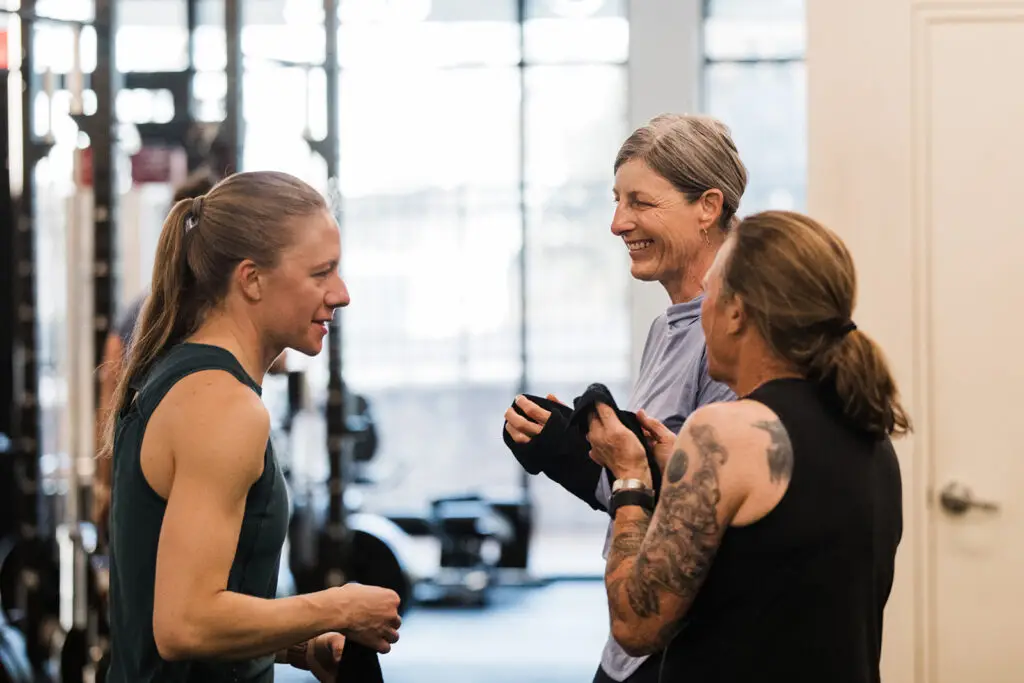 Three women talking and laughing in a strength class.