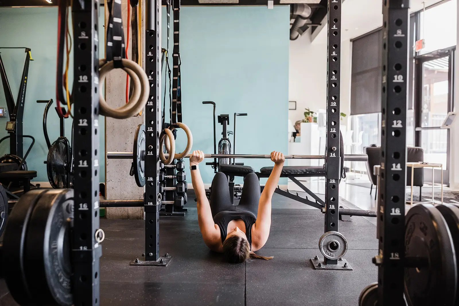 Woman performing a barbell floor press in a brightly lit gym.