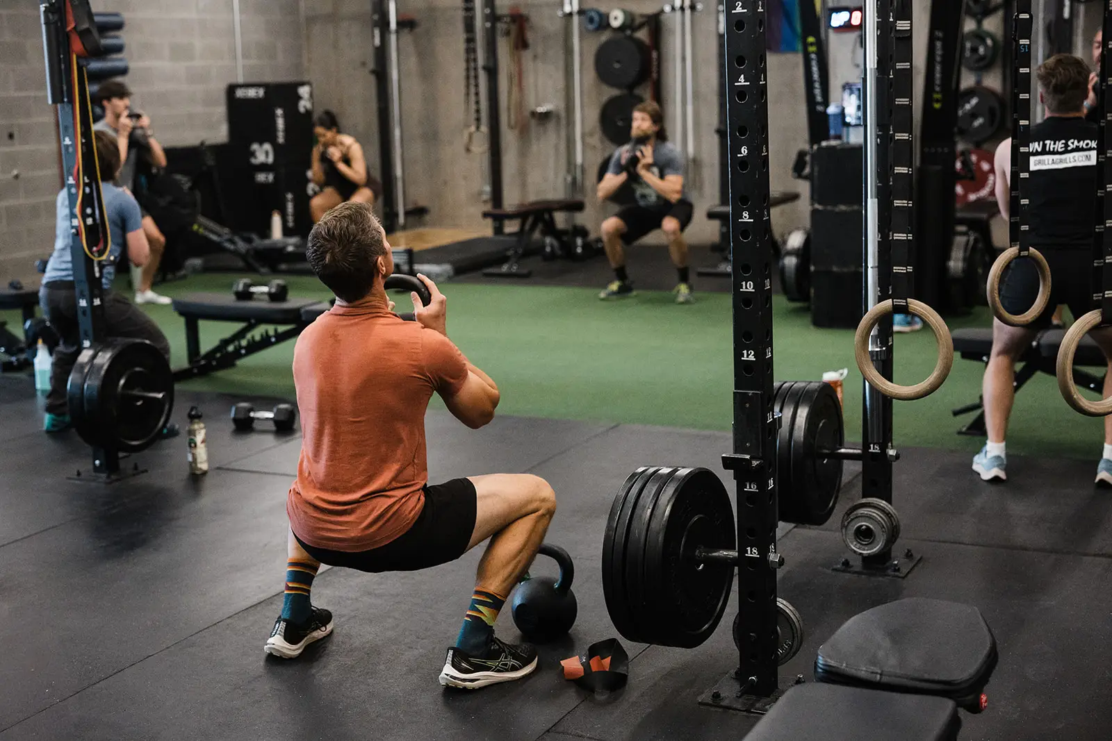 An athlete performing a goblet squat in the foreground, with several others performing the movement in the background