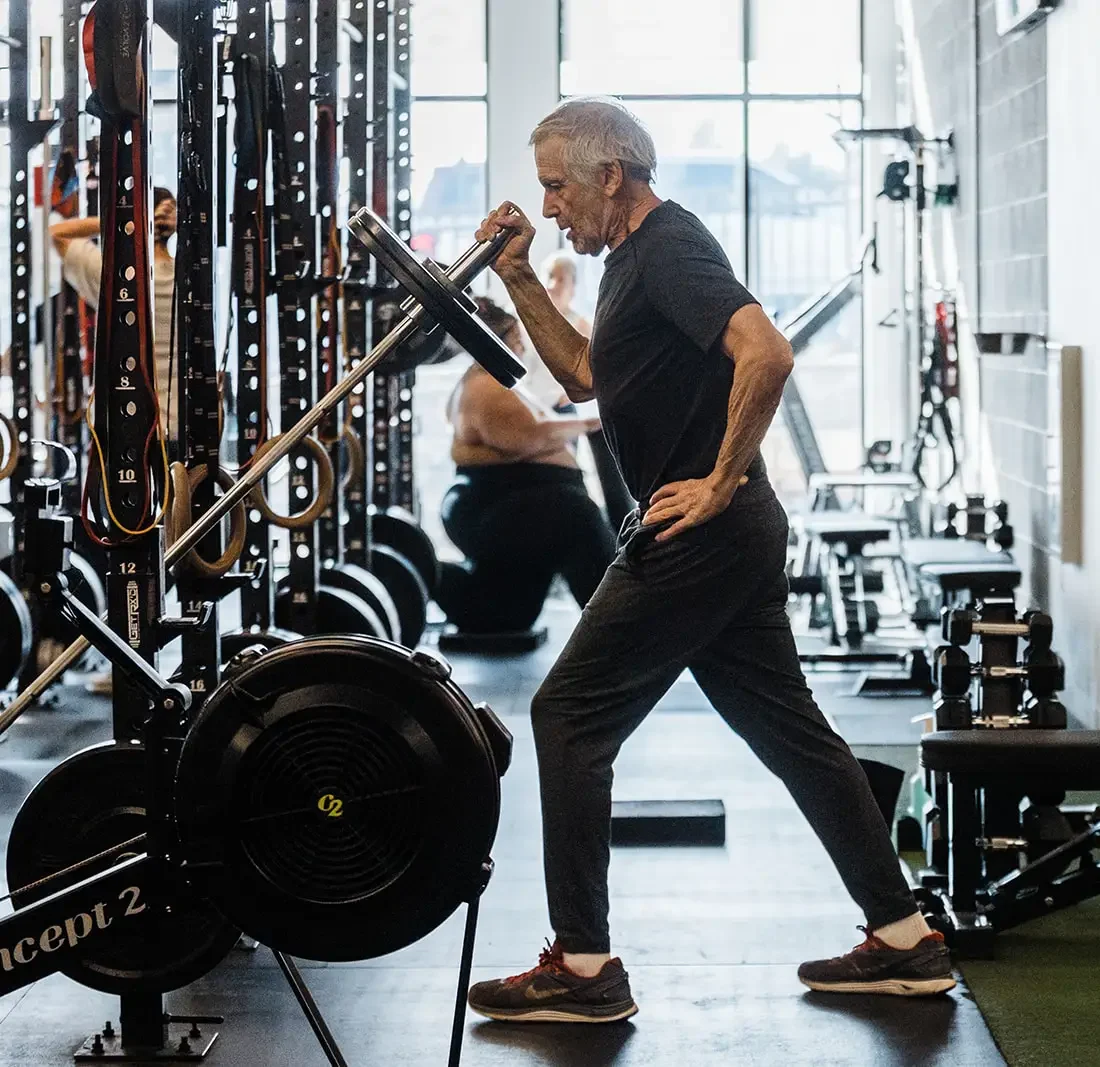 Older male performing a barbell landmine press in a gym
