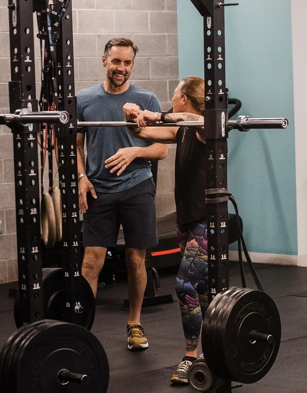 A male and female athlete chatting and laughing at a squat rack