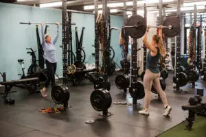 Three female athletes performing a barbell overhead press in a gym setting