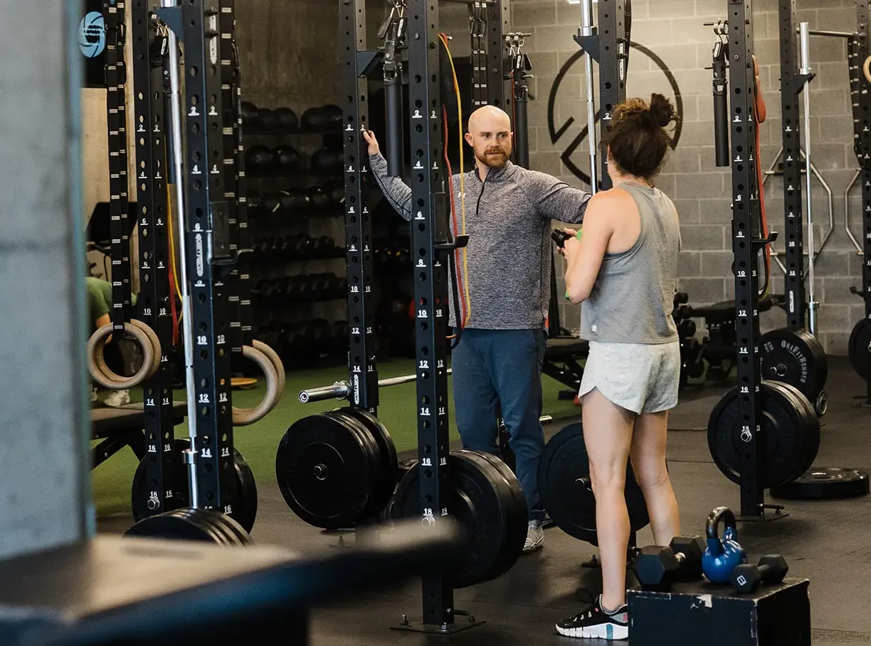 A male strength coach talking with a middle-aged female athlete.