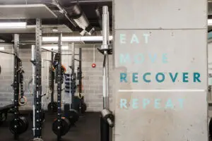 "Eat Move Recover Repeat" painted in teal on a concrete column at EVOLVE Flagstaff, with squat racks and gymnastics rings in the background