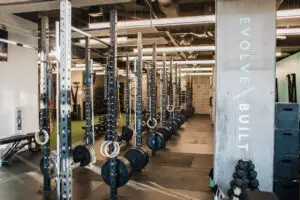 Squat racks and gymnastics rings at EVOLVE Flagstaff, with "EVOLVE Built" signage on a concrete column