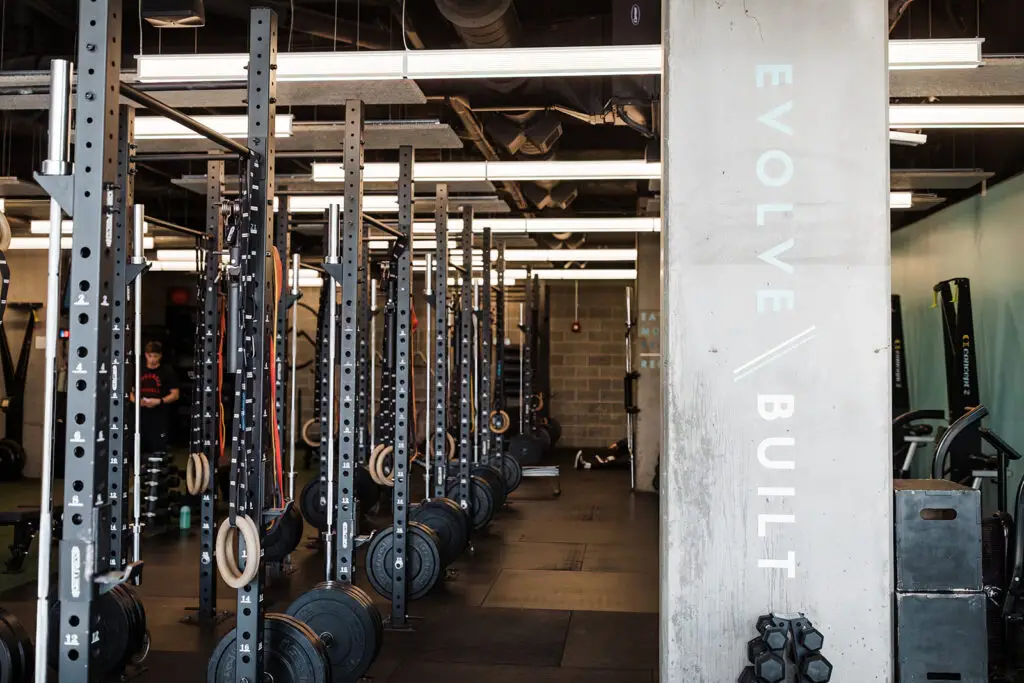"Evolve / Built" vertically on a concrete pillar in right foreground with squat racks in a row on right