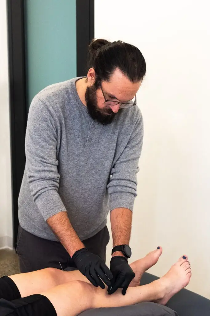 Male acupuncturist working on a patient's right shin and lower leg