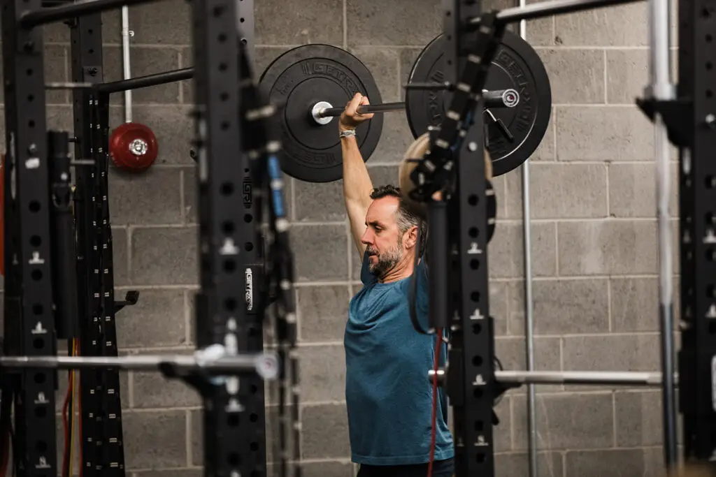 A man performing a barbell overhead press at the EVOLVE Flagstaff gym.